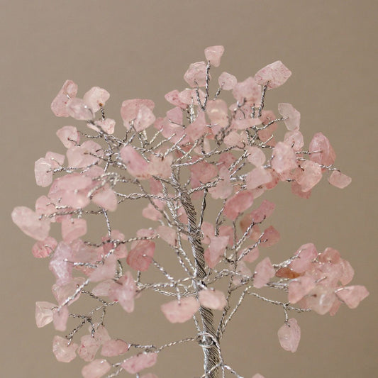 A decorative tree with a braided metal trunk displays numerous pink gemstone leaves against a neutral background.