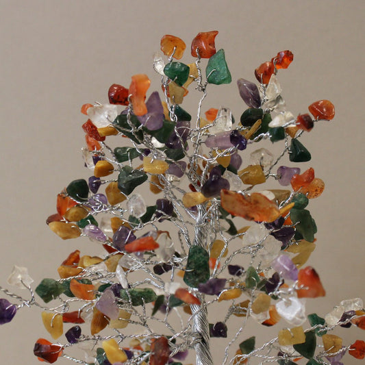 A gemstone tree made with silver wire branches stands against a neutral background. Colorful polished stones form the leaves.