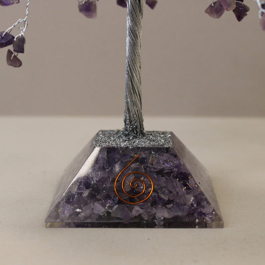 A wire gemstone tree sits on a trapezoidal base filled with amethyst. A copper spiral is embedded in the stone, against a neutral background.