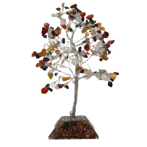 A decorative tree with a silver wire frame and colored gemstone "leaves" stands on a clear base filled with smaller stones, against a white background.