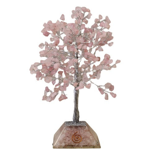 A tree sculpture, made of silver wire and rose quartz chips, sits on a clear, faceted crystal base featuring a copper spiral. The tree is centered against a white background.