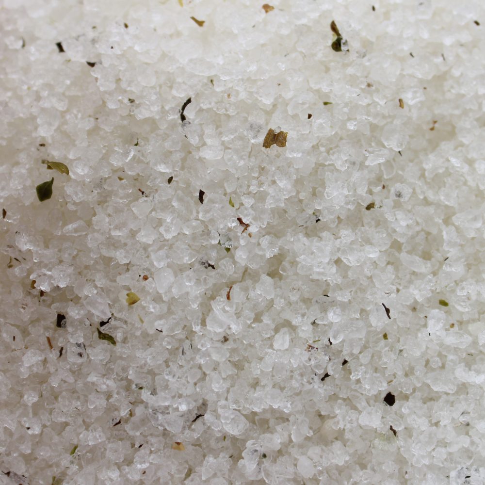Course sea salt crystals lay still, mixed with tiny, green and brown herb pieces, filling the frame.