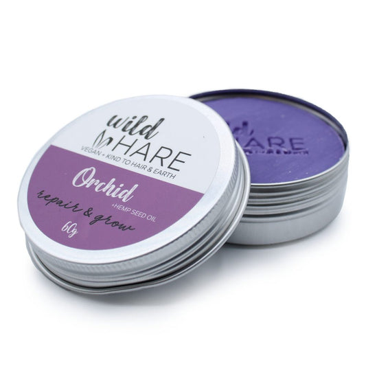 Small round metal tin of Wild Hare hair balm sits with lid partially removed revealing purple balm on a white background; Text: "wild HARE" "VEGAN + KIND TO HAIR & EARTH" "Orchid" "+HEMP SEED OIL" "repair & grow" "60g"