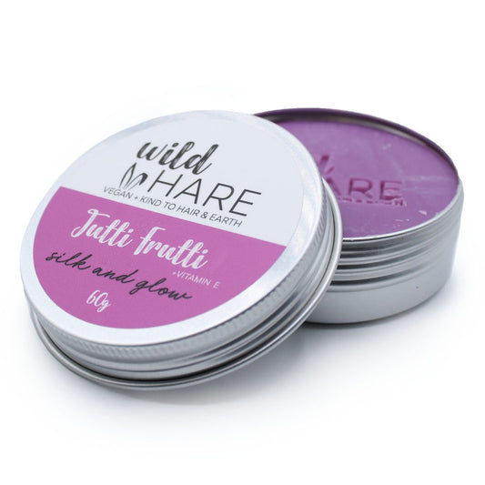 A round metal tin of hair balm with lid partly removed revealing purple balm on a white background; label reads wild HARE VEGAN + KIND TO HAIR & EARTH Tutti frutti silk and glow +VITAMIN E 60g