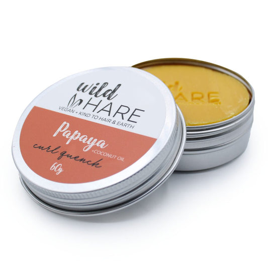 Small metal tin of hair balm with lid partially removed revealing yellow wax on a white background, Text: "wild HARE", "VEGAN + KIND TO HAIR & EARTH", "Papaya + COCONUT OIL", "curl quench", "60g", embossed "HARE" on wax.