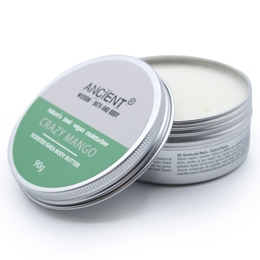 Two silver tins, one opened and one with the lid next to it, show “ANCIENTⓇ WISDOM - BATH AND BODY nature's best vegan moisturiser CRAZY MANGO SCENTED SHEA BODY BUTTER 90g” and other text on a white surface.