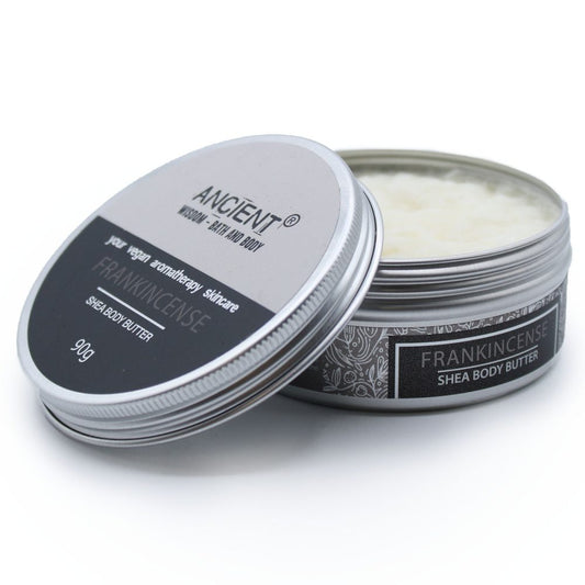 A round tin of Frankincense shea body butter with the lid partly removed revealing creamy butter on a white surface; text on tin: ANCIENT® WISDOM · BATH AND BODY your vegan aromatherapy skincare FRANKINCENSE SHEA BODY BUTTER 90g