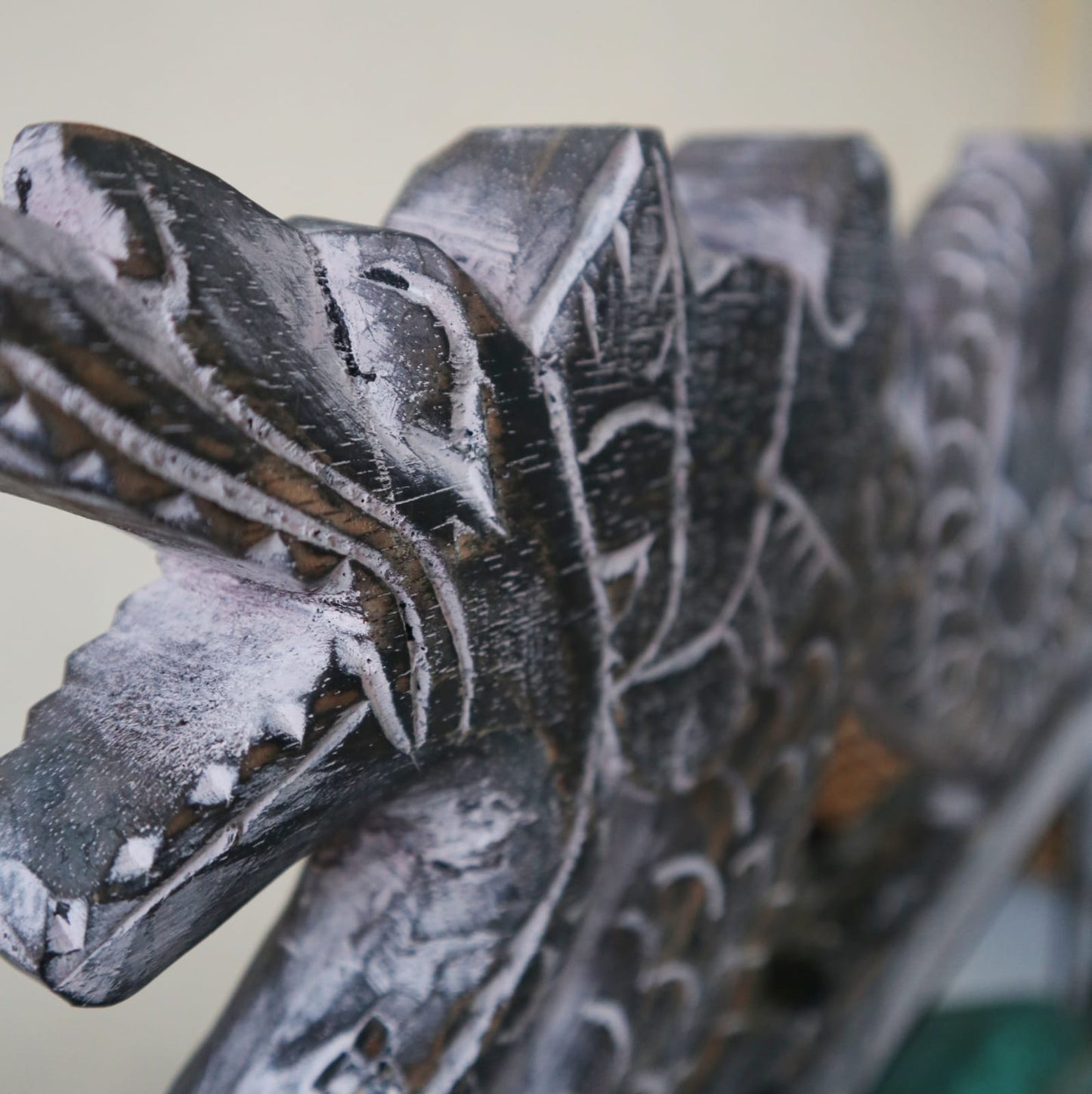 A detailed wooden carving of a dragon's face shows sharp teeth and intricate patterns, set against a plain, light background.