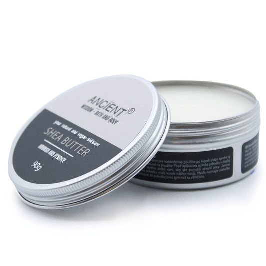 A round metal tin of shea butter sits open on a white surface, lid tilted forward reading: ANCIENT ® HOMME - BATH AND BODY pure natural and vegan skincare SHEA BUTTER NOURISH AND HYDRATE 90g.