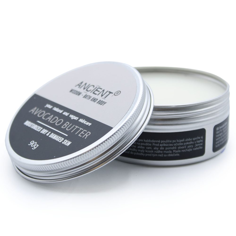 A silver tin of "ANCIENT Avocado Butter" skin cream sits open, lid slightly off, on a white surface. The label reads "your natural and vegan skincare. MOISTURIZES DRY & DAMAGED SKIN."