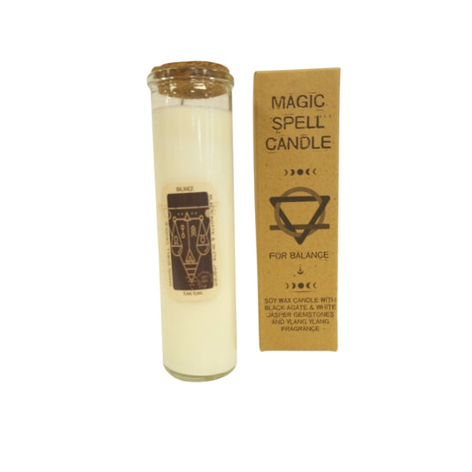 Glass-encased white candle stands upright beside a kraft cardboard box on a white background; candle label reads BALANCE and box reads MAGIC SPELL CANDLE FOR BALANCE SOY WAX CANDLE WITH BLACK AGATE & WHITE JASPER GEMSTONES AND YLANG YLANG FRAGRANCE.