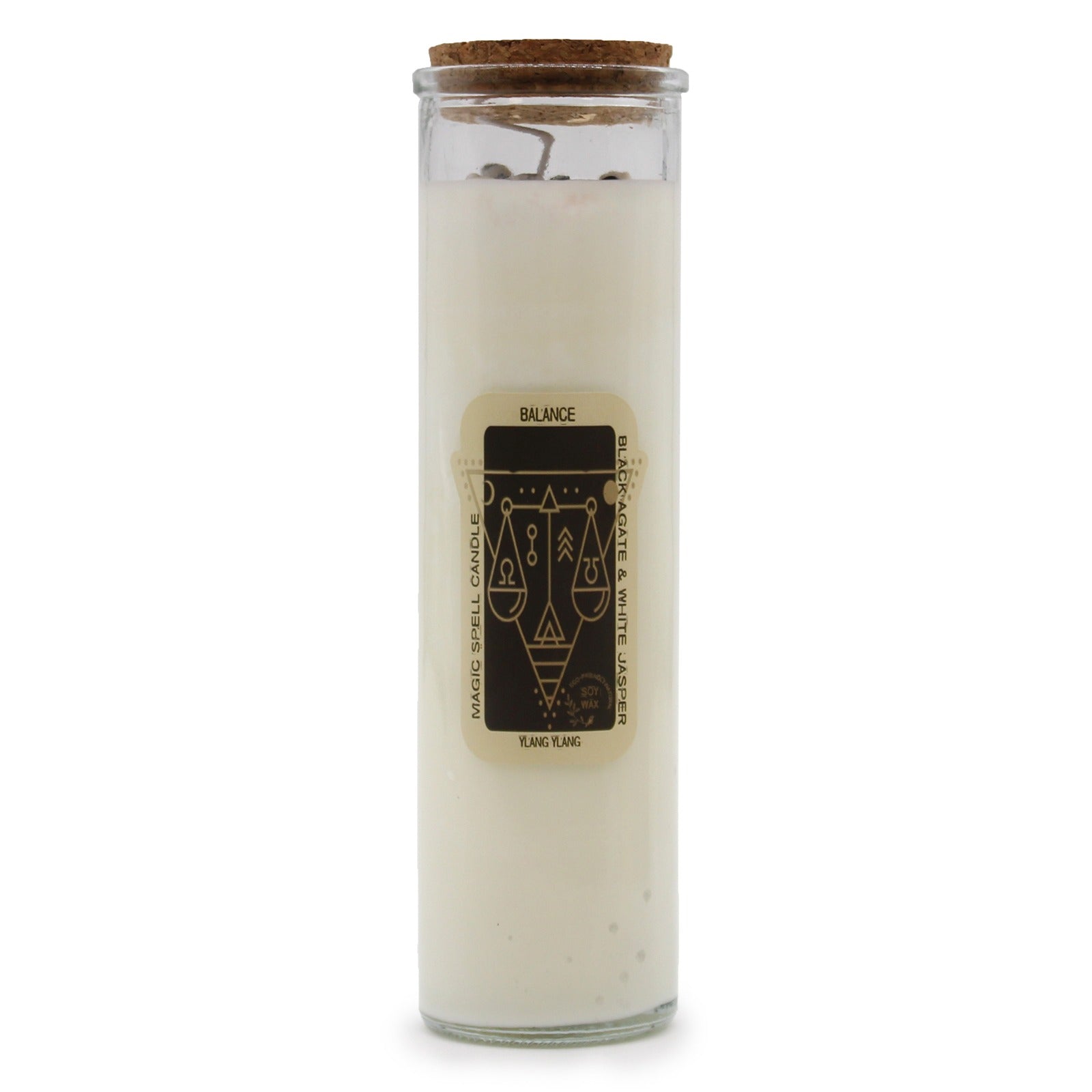 A glass-encased candle, topped with a cork lid, sits on a white surface. The candle has a cream wax filling and a label that reads "BALANCE. MAGIC SPELL CANDLE, BLACK AGATE & WHITE JASPER, YLANG YLANG".