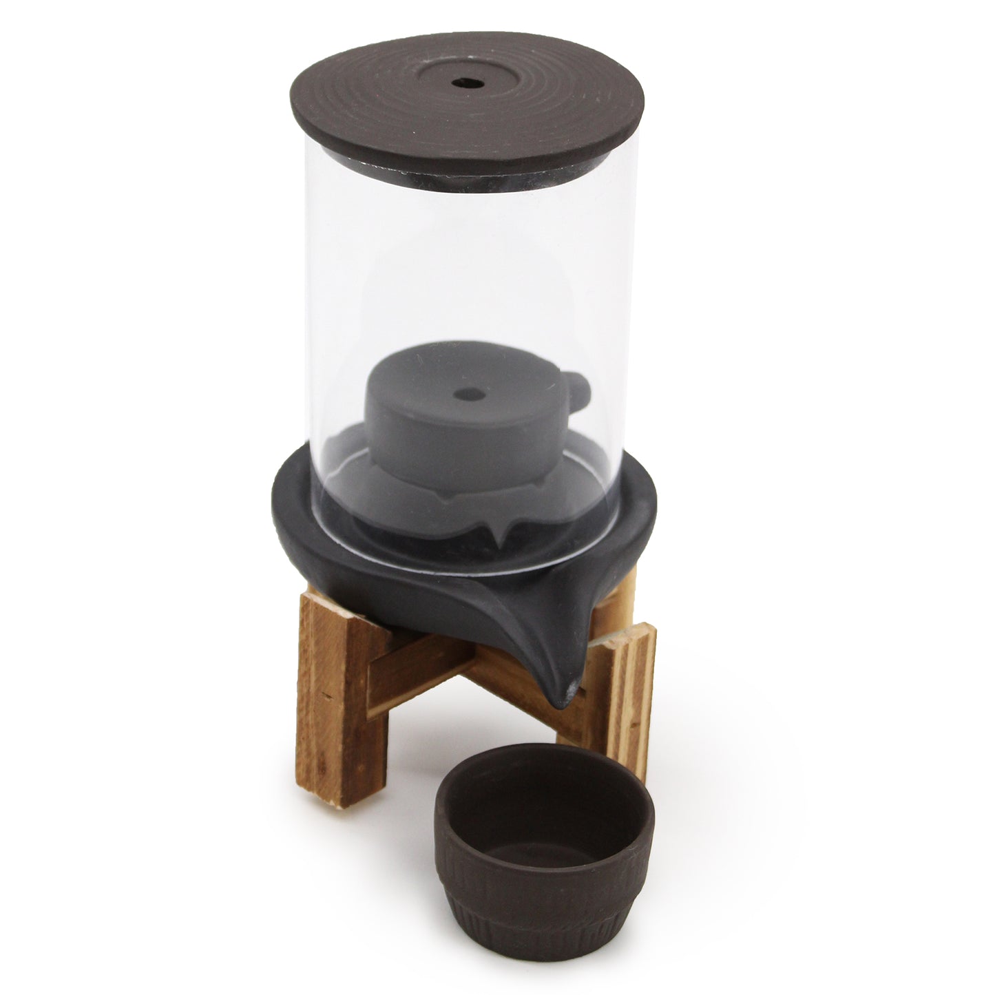 A glass vacuum coffee maker stands on a wooden tripod, with a black lid and filter, and an empty black cup placed beside it on a plain white background.