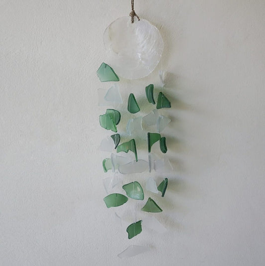 A seashell-topped mobile hangs from a wall, featuring numerous green and frosted glass pieces dangling below.