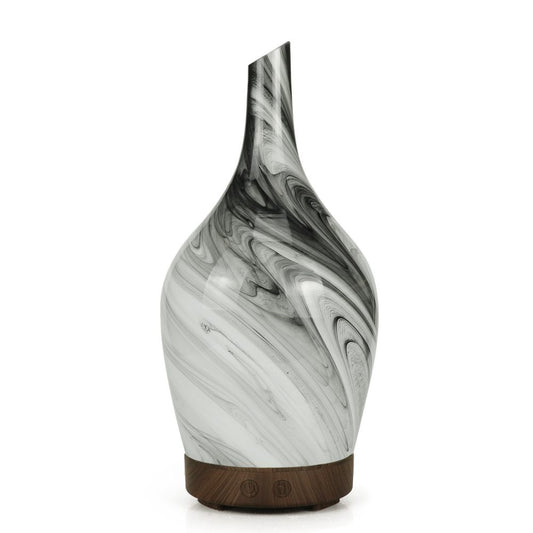 A black and white marbled glass diffuser stands on a circular wooden base, featuring two symbols. It’s isolated against a bright white backdrop.