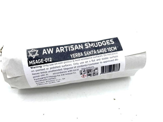 A wrapped smudge stick sits on a white surface. The packaging reads "AW ARTISAN SMUDGES MSAGE-012 YERBA SANTA SAGE 10CM". Warning labels and other informational text are also on the packaging.