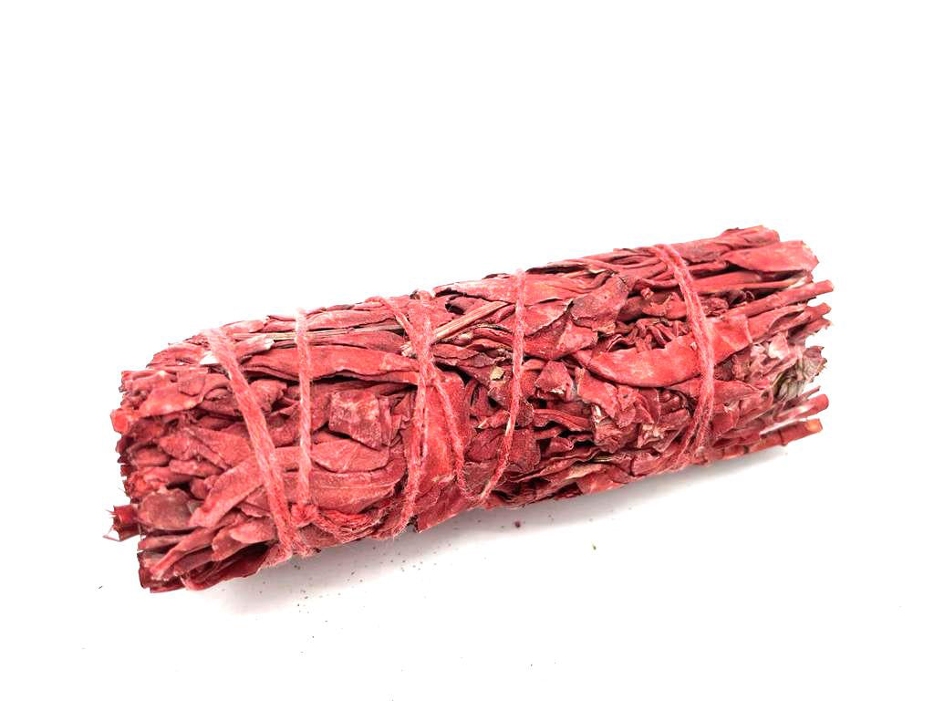 A red sage smudge stick, bound with twine, rests on a white surface.