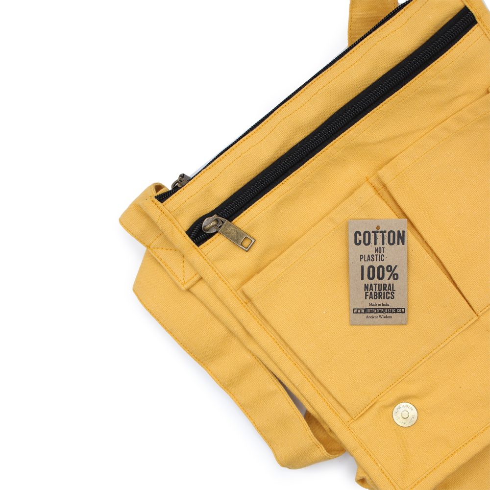 A golden-yellow cotton bag with a black zipper rests on a white surface, its tag reading "COTTON NOT PLASTIC 100% NATURAL FABRICS Made in India WWW.JUTENOTPLASTIC.COM Ancient Wisdom."