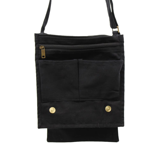 A black canvas bag hangs, featuring a zipped top compartment, two front pockets, and a fold-down flap secured by two brass-colored snaps, all against a white background.