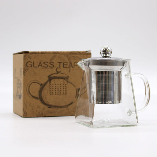 A transparent glass teapot with a metal infuser and lid is positioned next to a cardboard box labeled "GLASS TEA." The box features an illustration of a teapot.