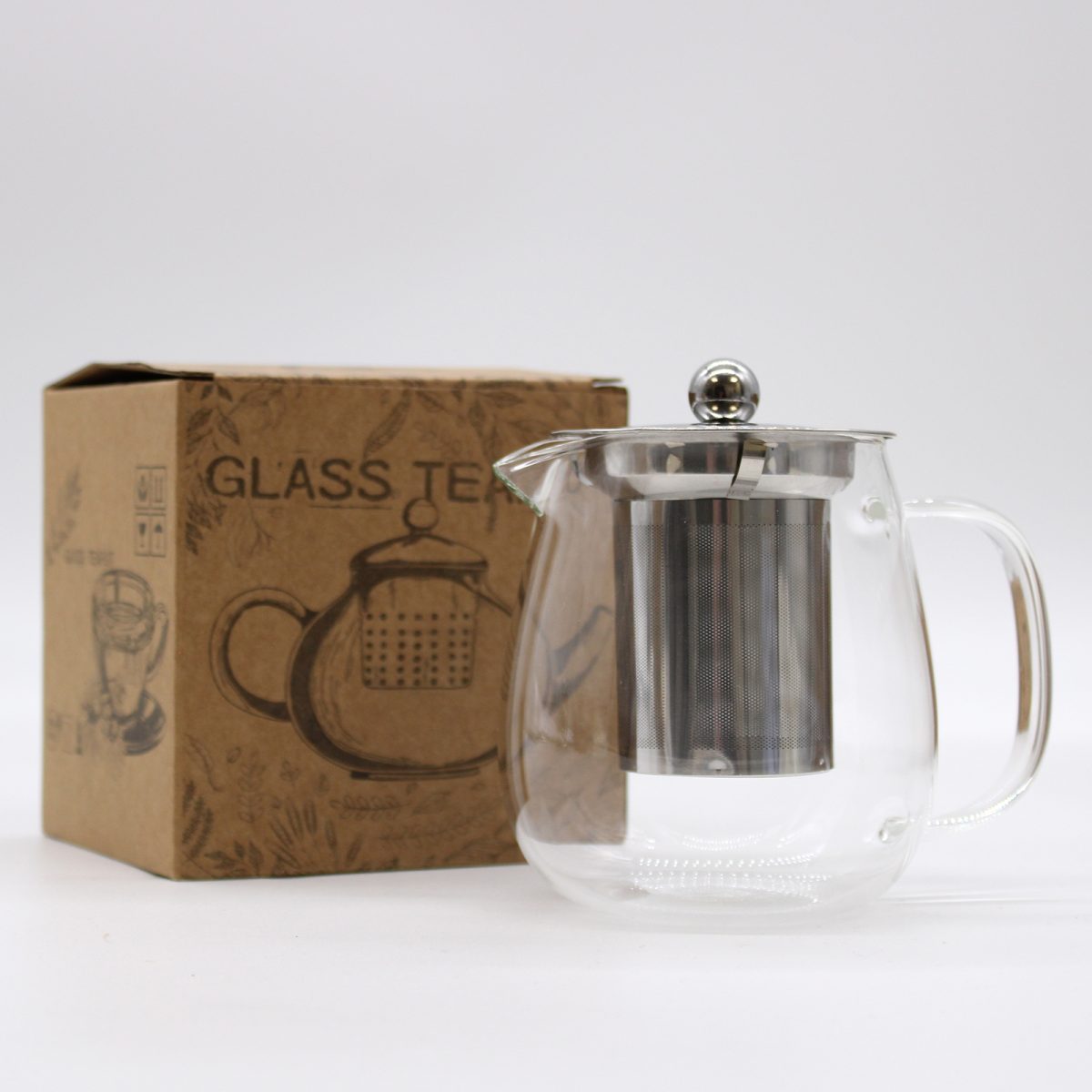 A clear glass teapot with a metal infuser and lid is placed beside a brown box labeled "GLASS TEA," featuring illustrations of a teapot. The background is plain white.