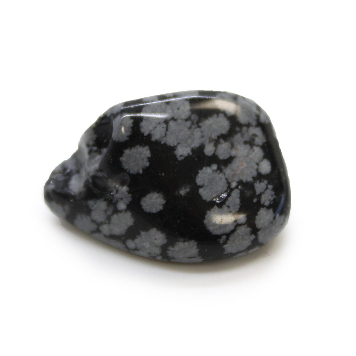 A polished snowflake obsidian stone sits on a white surface. The stone has a mostly dark gray, nearly black, base color with light gray, flower-like inclusions.