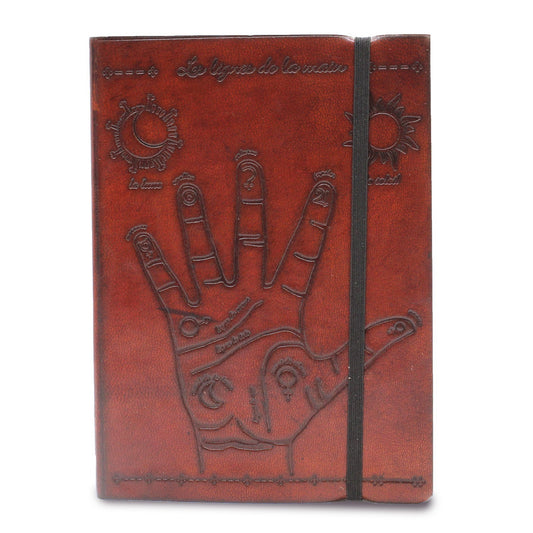 A brown journal with a black elastic band displays a palm reading diagram including planets and phrases such as “les lignes de la main,” "la lune", and “le soleil.”