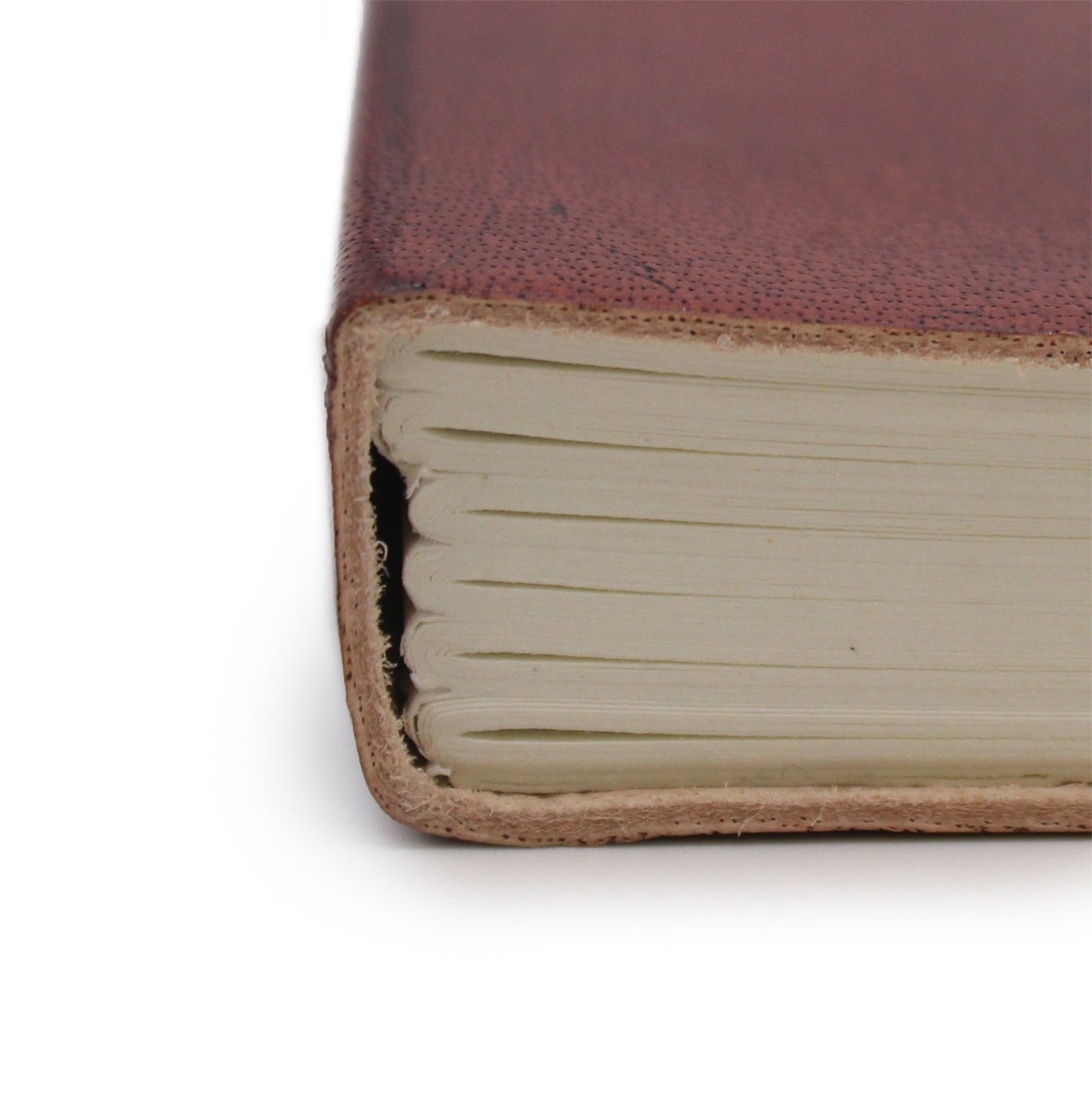 A tan leather-bound notebook lays on a white surface. The spine with visible pages is facing the viewer.