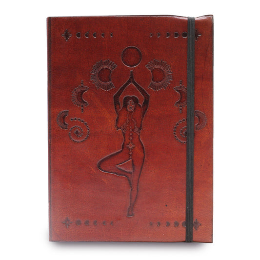 The leather journal features a debossed design of a woman doing tree pose under a sun, flanked by moons and stars, with a black elastic band.