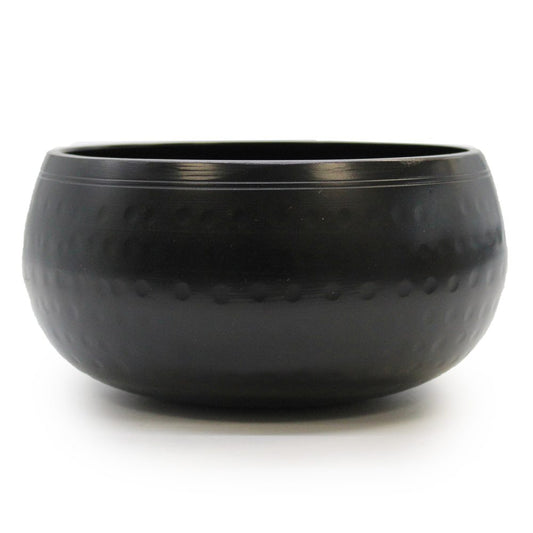 A matte black bowl with a smooth, rounded shape and subtle textured dots sits on a plain white surface, suggesting simplicity and elegance in its design.