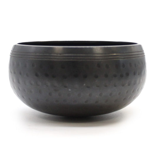A textured black bowl rests on a plain white surface, featuring a smooth rim and dotted exterior, creating a simple yet elegant appearance.