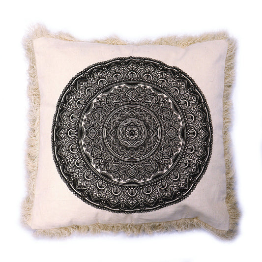 A beige square pillow displays a large, black mandala design. The pillow has a light beige fringe.