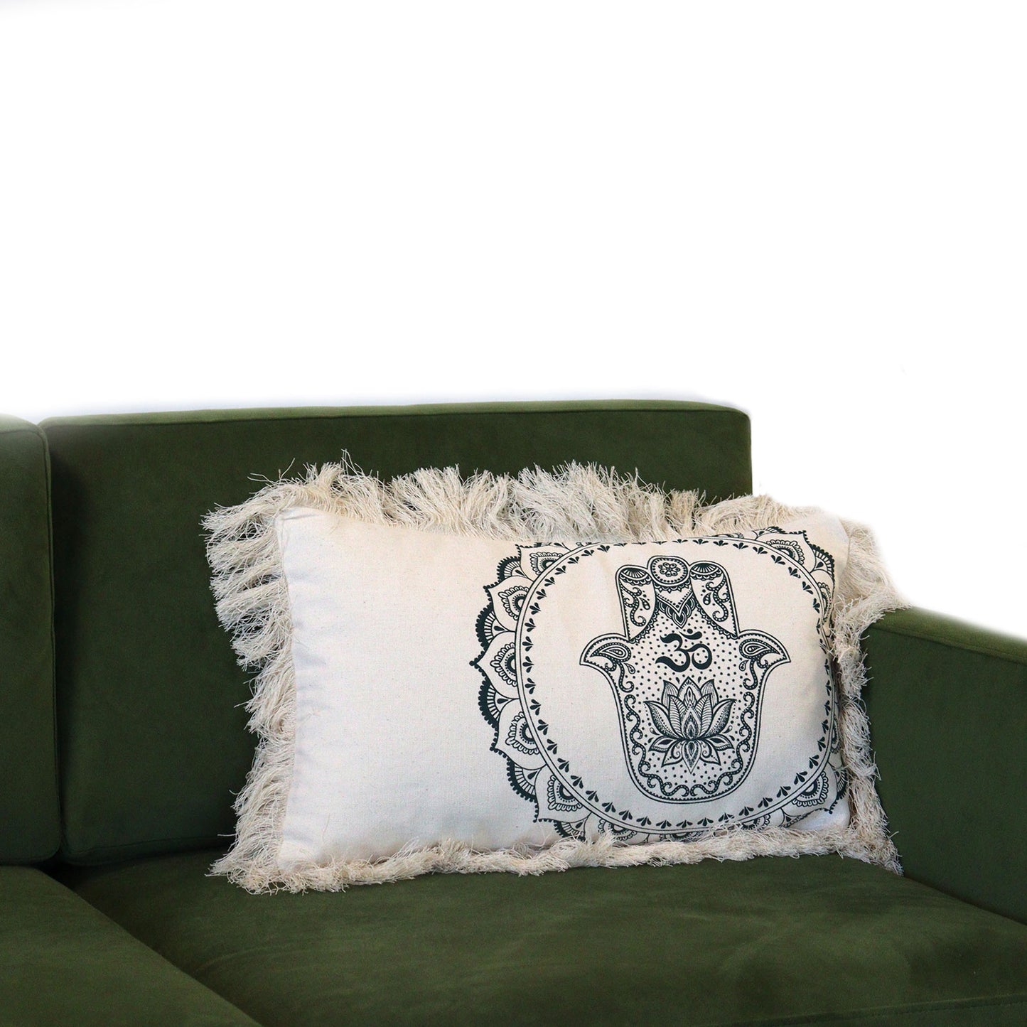 A fringed beige pillow, featuring a black Hamsa design, rests on a dark green sofa.