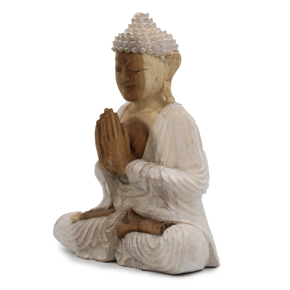 A carved wooden Buddha statue sits cross-legged, hands in prayer, wearing a flowing robe. Its serene expression communicates peace, with textured detailing on its hair and robe.