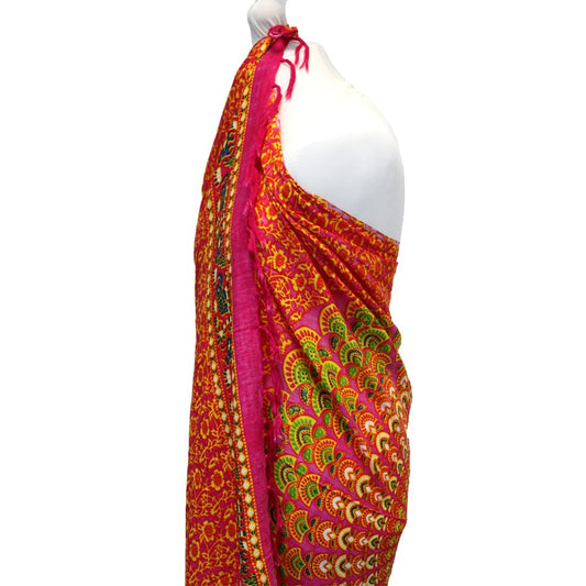 A pink and gold sarong, draped on a mannequin, displays a peacock feather pattern.