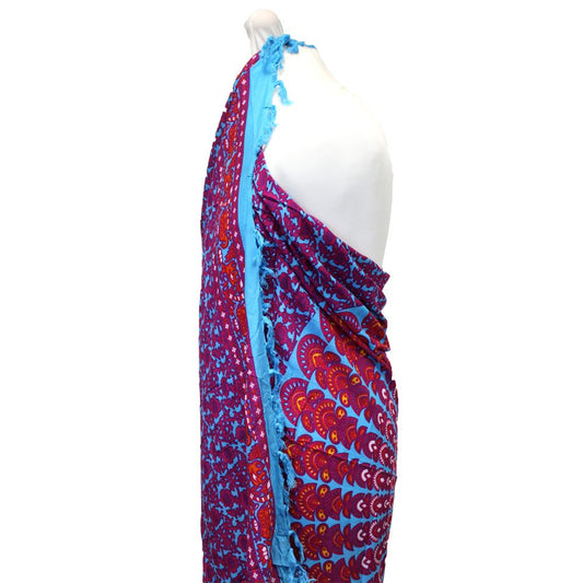 A patterned sarong, draped over a mannequin, displays vibrant purple and orange mandala designs on a turquoise background.