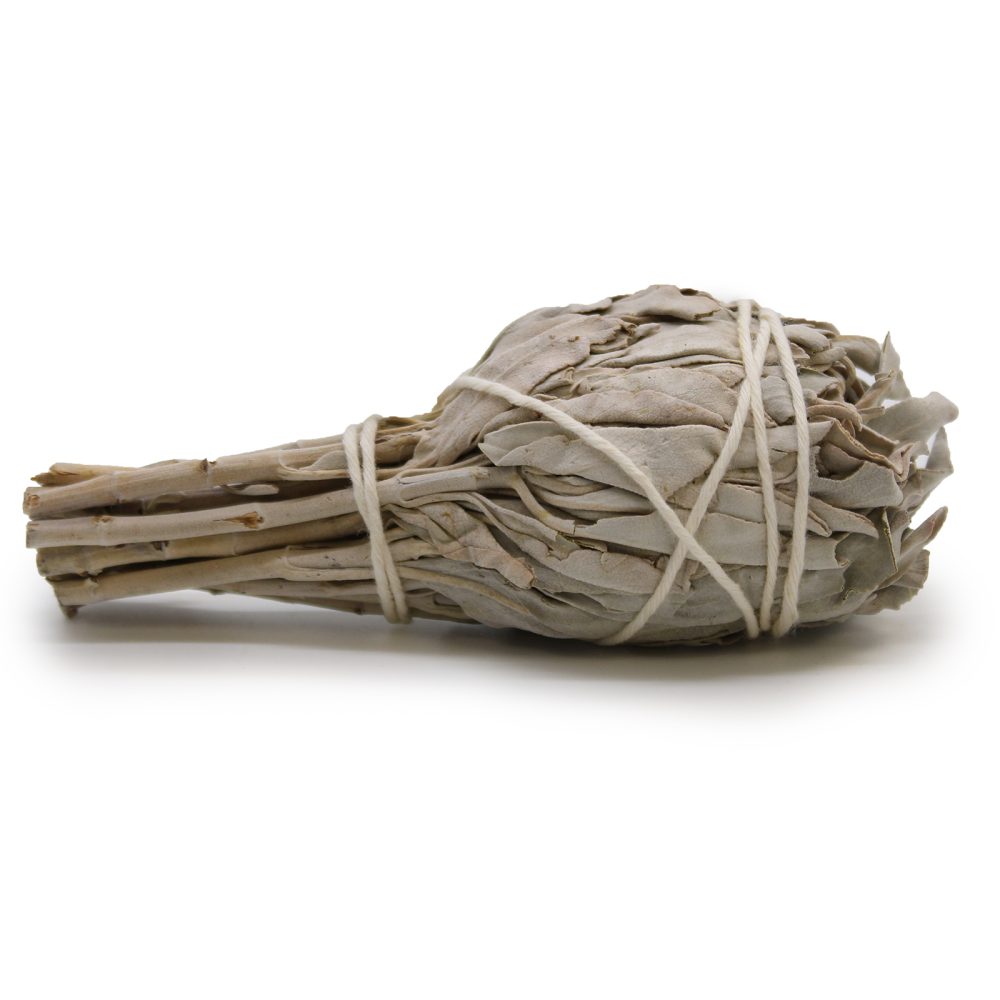 A bundle of dried white sage, tied with twine, rests on a white surface.