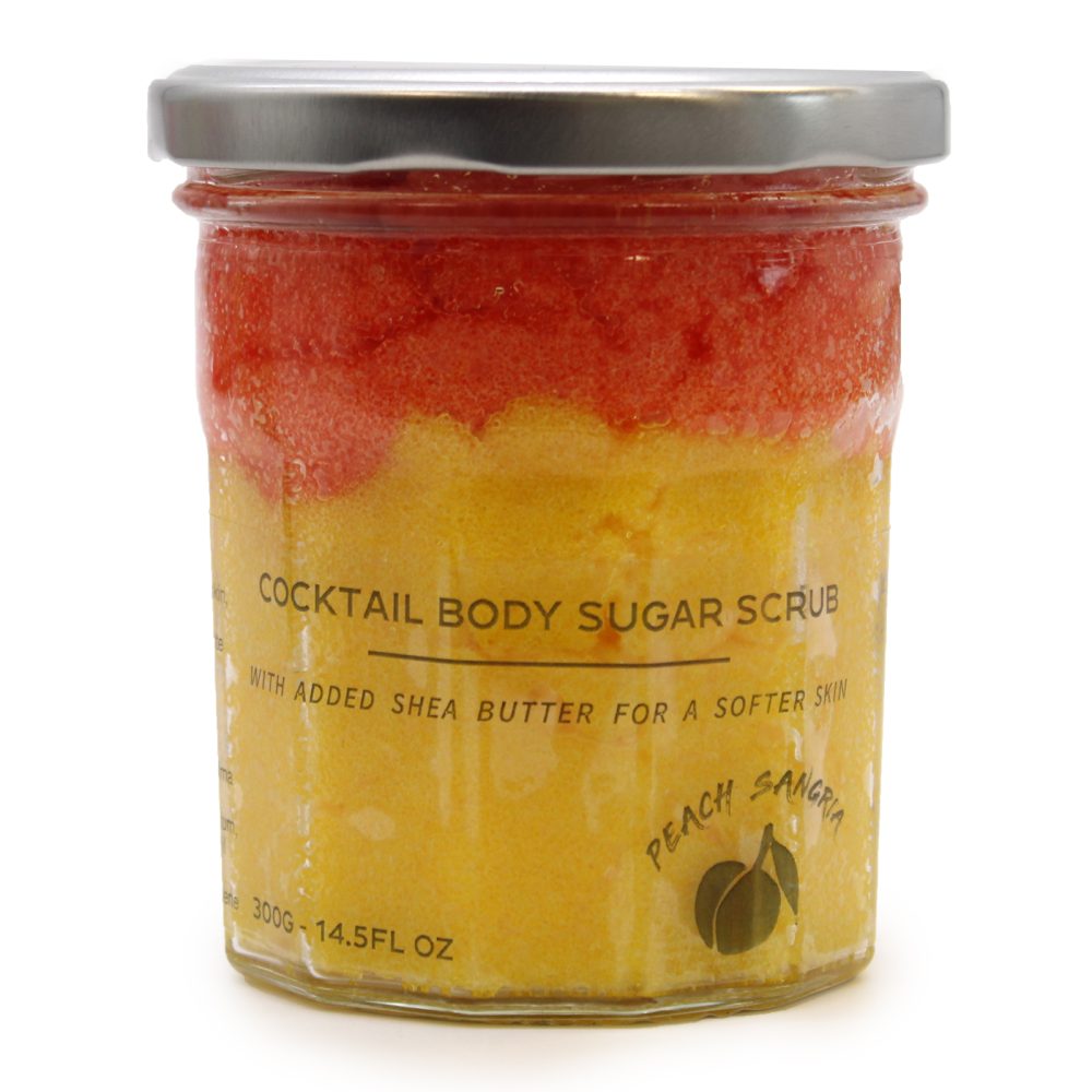 A jar of "COCKTAIL BODY SUGAR SCRUB," with added shea butter, sits on a white surface. The scrub is layered red and yellow. The label says "PEACH SANGRIA," and "300G-14.5FL OZ".