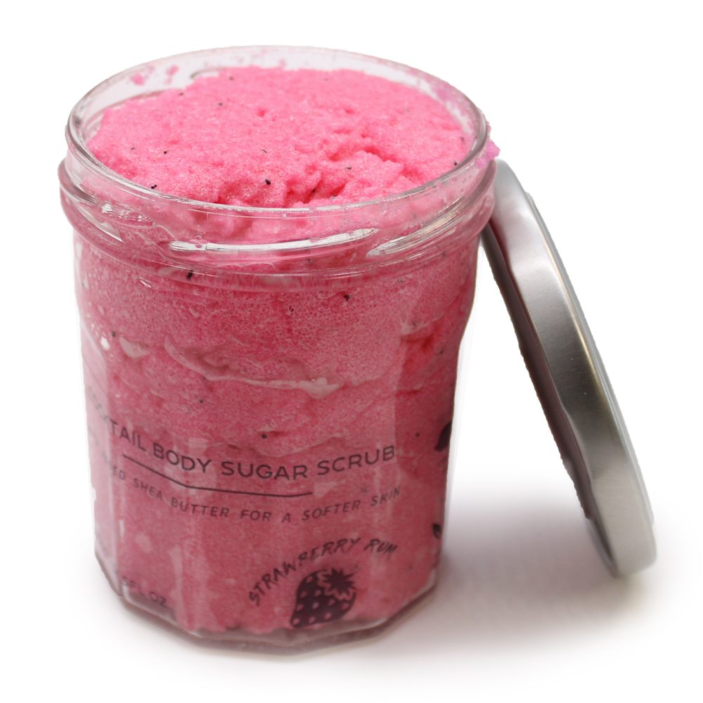 The open jar of pink body scrub with "COCKTAIL BODY SUGAR SCRUB, ADDED SHEA BUTTER FOR A SOFTER SKIN, STRAWBERRY RUM" text sits next to its silver lid against a white backdrop.