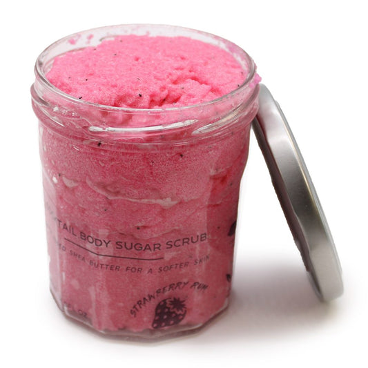 Glass jar of bright pink body scrub sits open beside a metal lid on a white surface; visible text: "TAIL BODY SUGAR SCRUB" "ED SHEA BUTTER FOR A SOFTER SKIN" "STRAWBERRY PUM" "FL OZ".