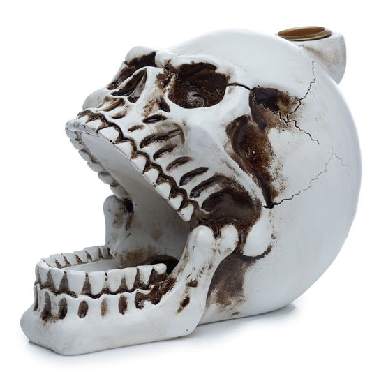 A ceramic object shaped like a skull with an open mouth and cracks is displayed against a plain white background. The skull is decorated with darkened grooves and details.