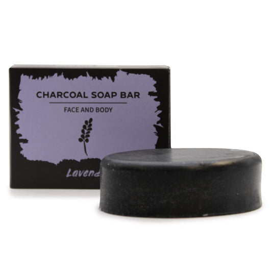 A black oval charcoal soap bar sits in front of a purple-labeled box on a white background; box text reads: CHARCOAL SOAP BAR FACE AND BODY Lavender.