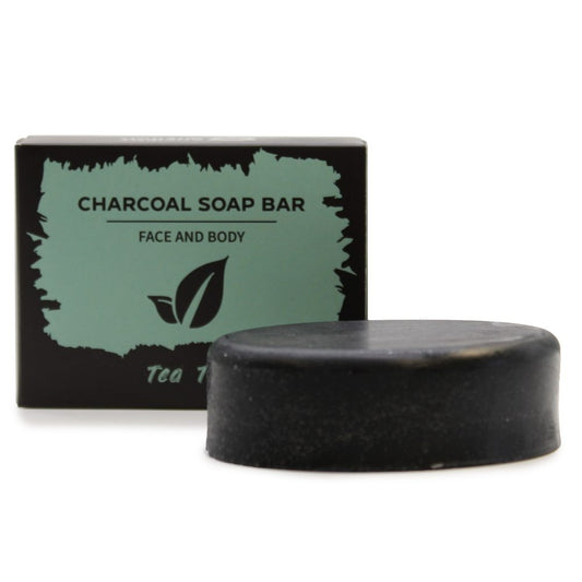 A round black charcoal soap bar sits before a boxed package labeled CHARCOAL SOAP BAR FACE AND BODY with a leaf logo and the partial text "Tea T".