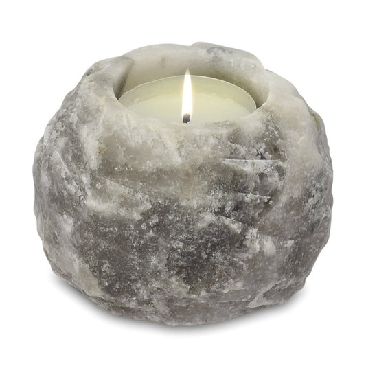 A lit tealight candle is placed within a rough, grey stone holder. The flame flickers gently, surrounded by the textured surface of the natural rock material.