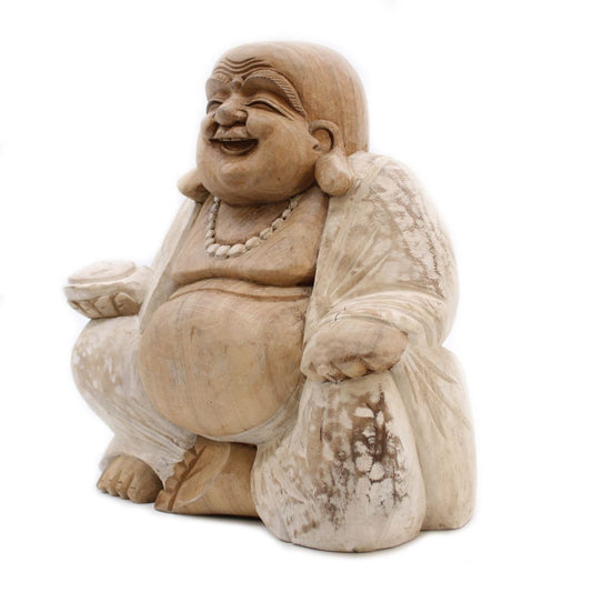 A wooden sculpture depicting a laughing, seated figure with a round belly, wearing a robe and necklace, set against a plain white background.