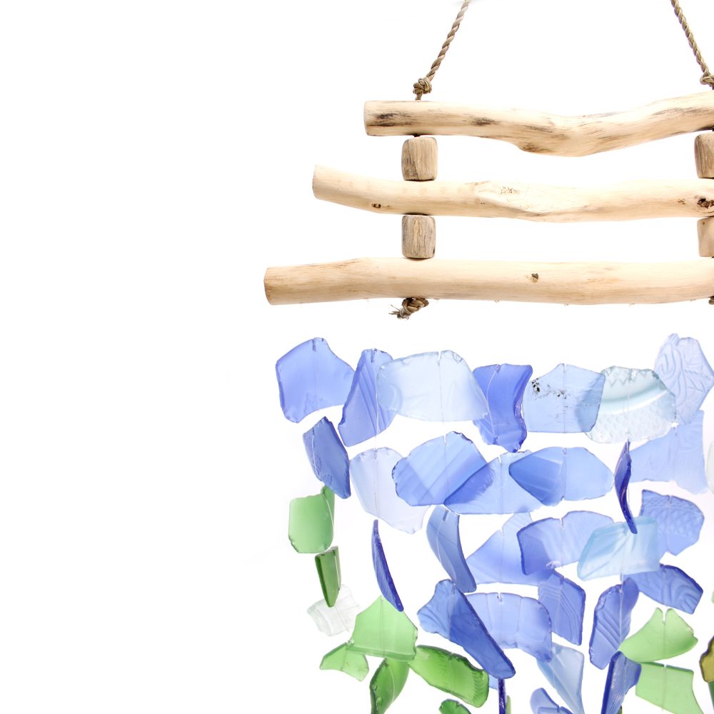 A driftwood-framed wind chime hangs, showcasing numerous blue and green glass shards that gently dangle.