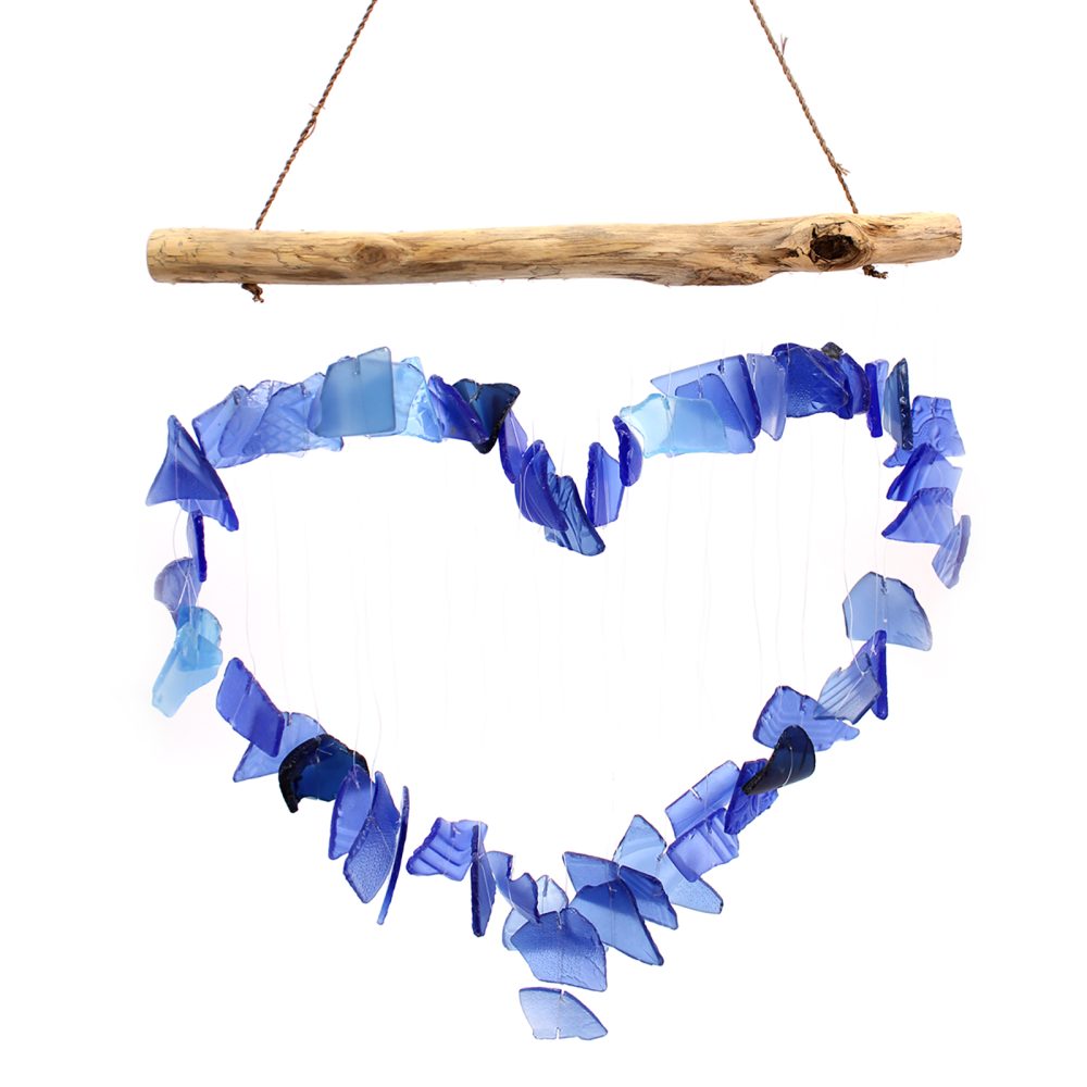 A heart-shaped wind chime hangs from a driftwood branch. Blue glass pieces form the heart, suspended by thin strings.