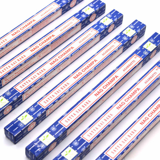 Incense boxes labeled "Satya Sai Baba Nag Champa Agarbatti" are arranged diagonally on a white surface. The packaging is blue with red and white text, featuring circular and leaf designs.