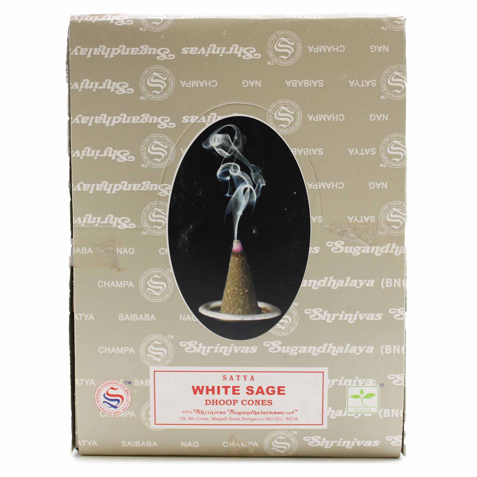 A burning incense cone releases wisps of smoke upward. The box, labeled "Satya White Sage Dhoop Cones," features decorative branding and an oval window displaying the smoking cone.