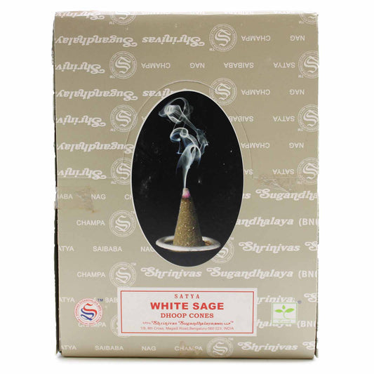 A burning incense cone releases wisps of smoke upward. The box, labeled "Satya White Sage Dhoop Cones," features decorative branding and an oval window displaying the smoking cone.